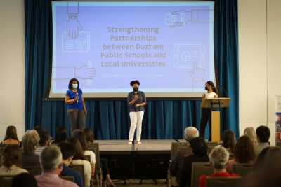 Three students on stage making a presentation.