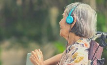 Woman with gray hair wearing headphones and sitting in wheelchair outdoors.