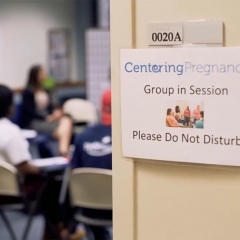 Image of classroom with sign reading "Centering Pregnancy Group in Session."