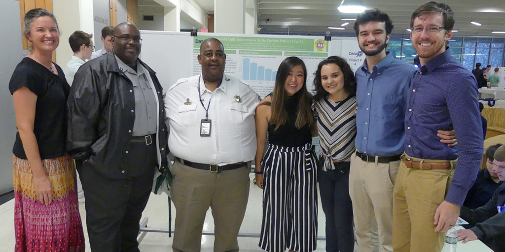 Data+ student team members and members of the Durham Crisis Intervention Team smile in front of their poster.