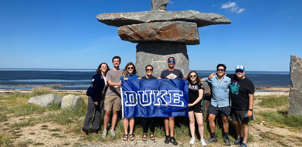 Members of the Belugas: Sentinels of Climate Change team posing in front of the ocean with a Duke University banner.