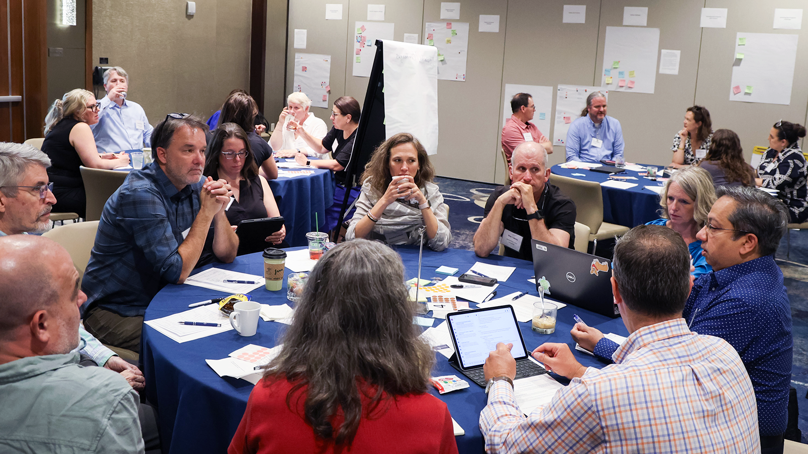 Groups of people seated at round tables discussing topics related to project-based learning in higher education during the symposium